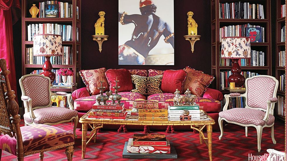 red and black and gold maximalist style sitting area with patterned sofa and chairs and leather bookshelves