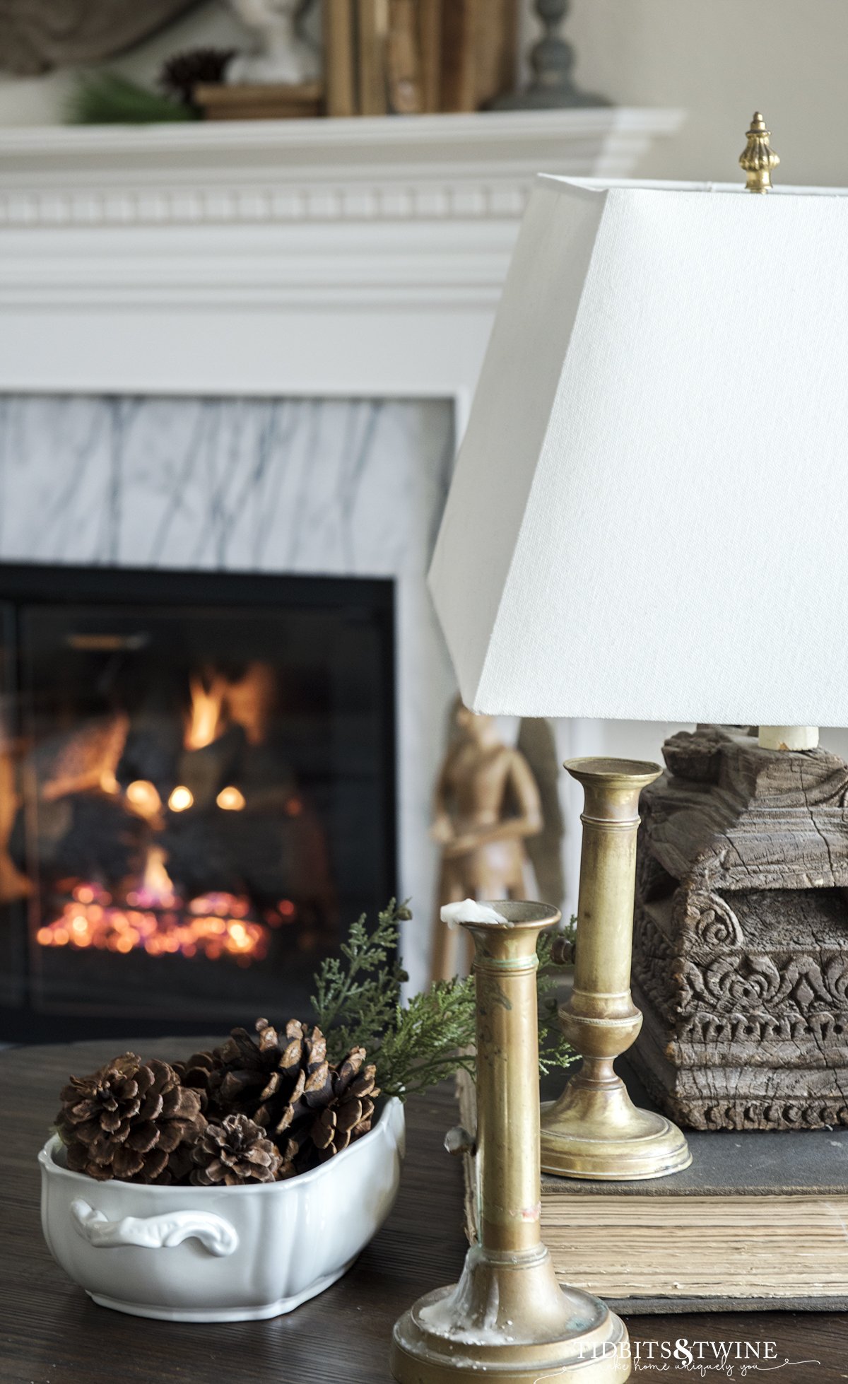 side table with vintage brass french candle sticks and ironstone tureen holding pinecones and fireplace in background