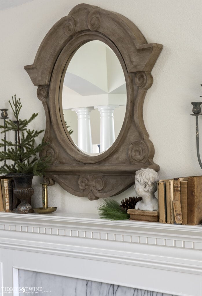 white and marble fireplace decorated for winter with evergreens and vintage books