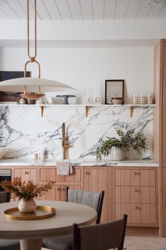 warm wood kitchen cabinets with marble counter and backsplash and gold finishes