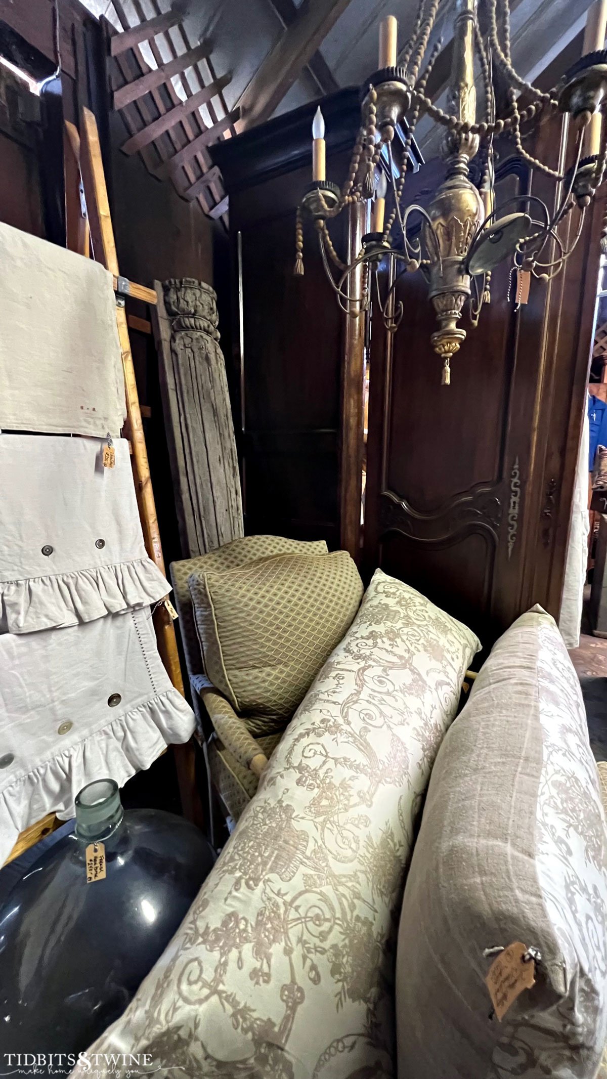 antique european linens and pillows stacked on a chair with a beaded french chandelier above