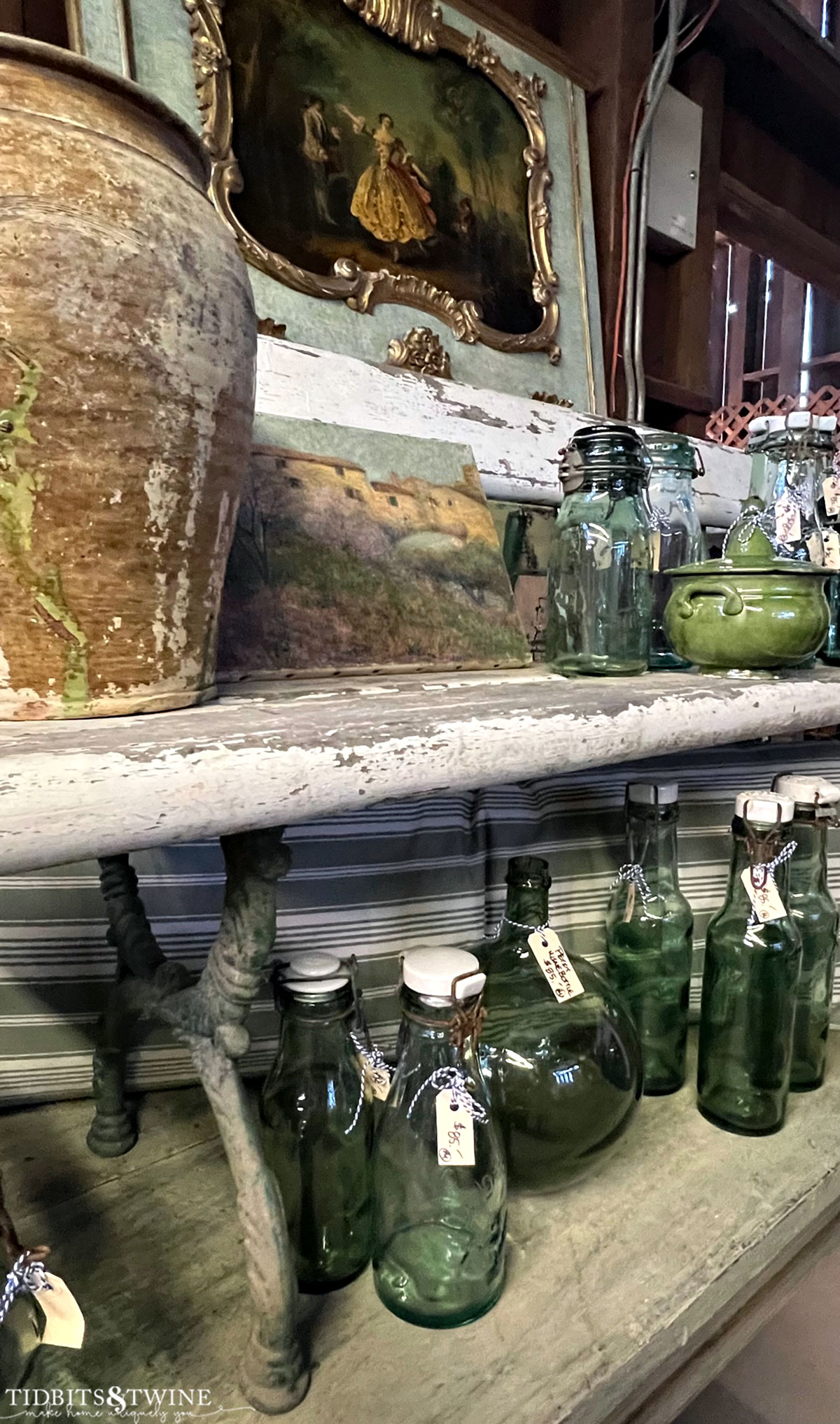 table with green glass bottles and green antique pottery an old white bench and a blue trumeau mirror