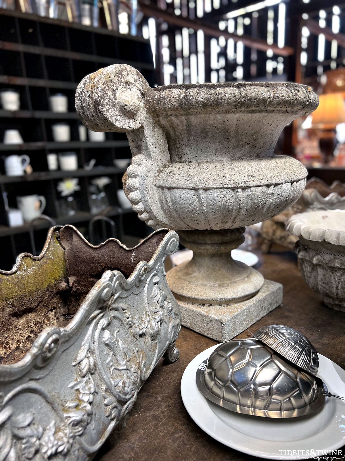 large antique cement urn on table next to french jardiniere and silver butter molds