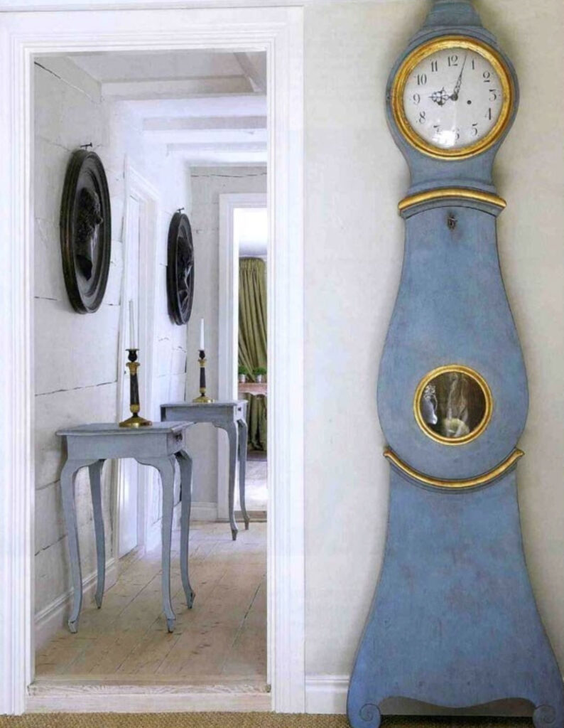 blue mora clock with gold accents against light beige wall next to doorway