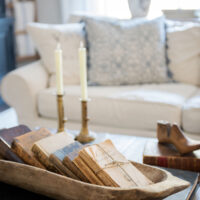 french coffee table styled with antique dough bowl full of old books with two brass candlesticks in background