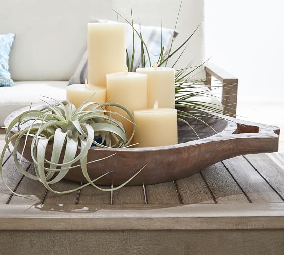 round dough bowl containing five candles and two air plants on outdoor coffee table