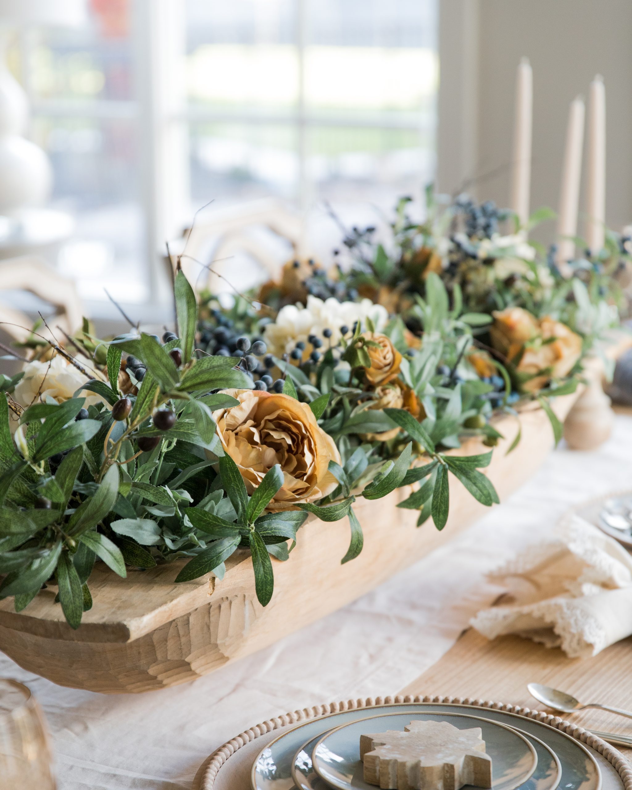 dough bowl centerpiece filled with faux olive stems white hydrangea and brown peonies on a dining table