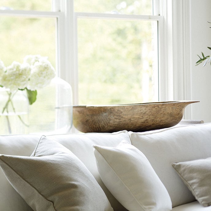 white sofa with table behind holding empty dough bowl clear demijohn and vase with white hydrangea