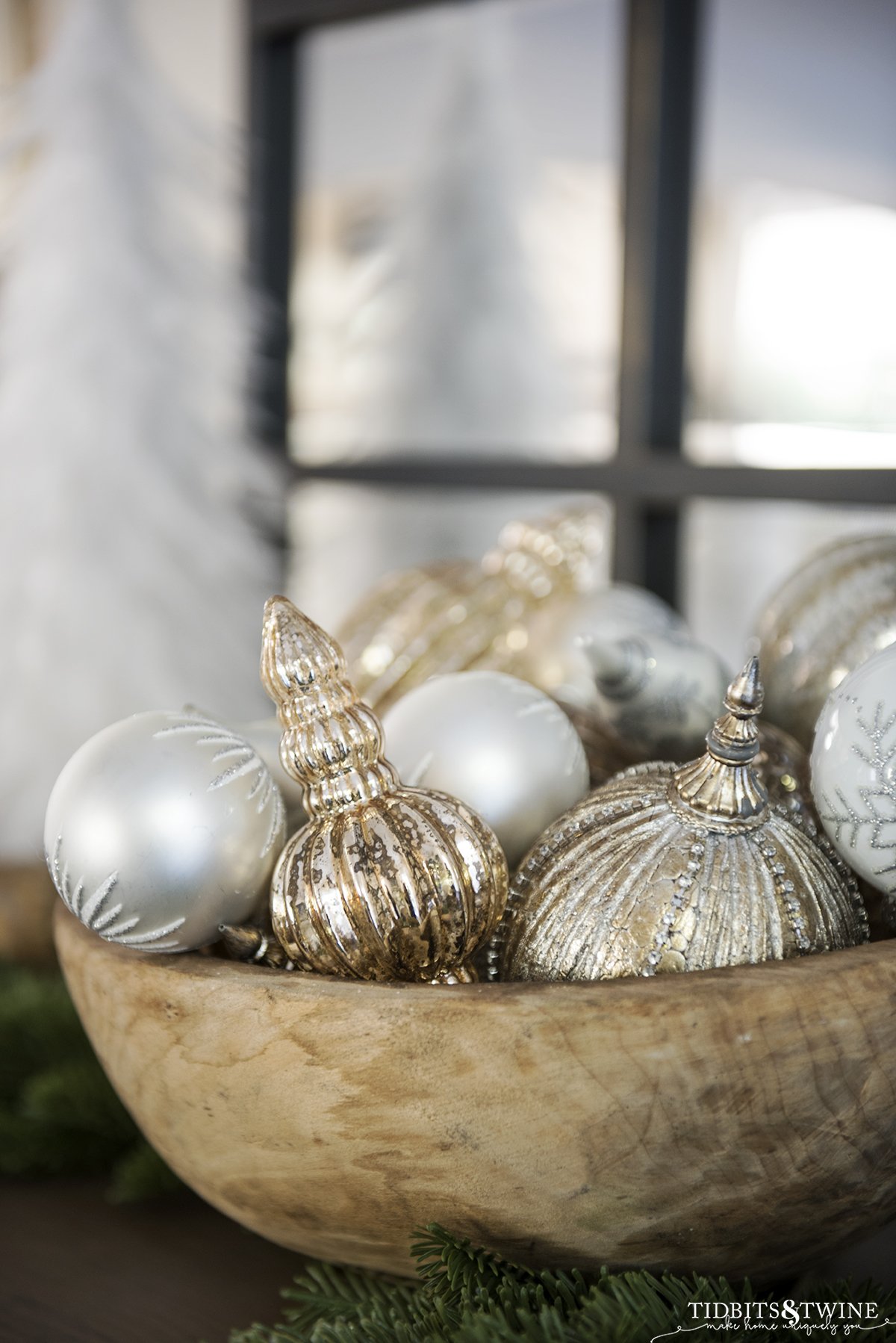 antique round dough bowl holding white silver and gold christmas ornaments with greenery at the base