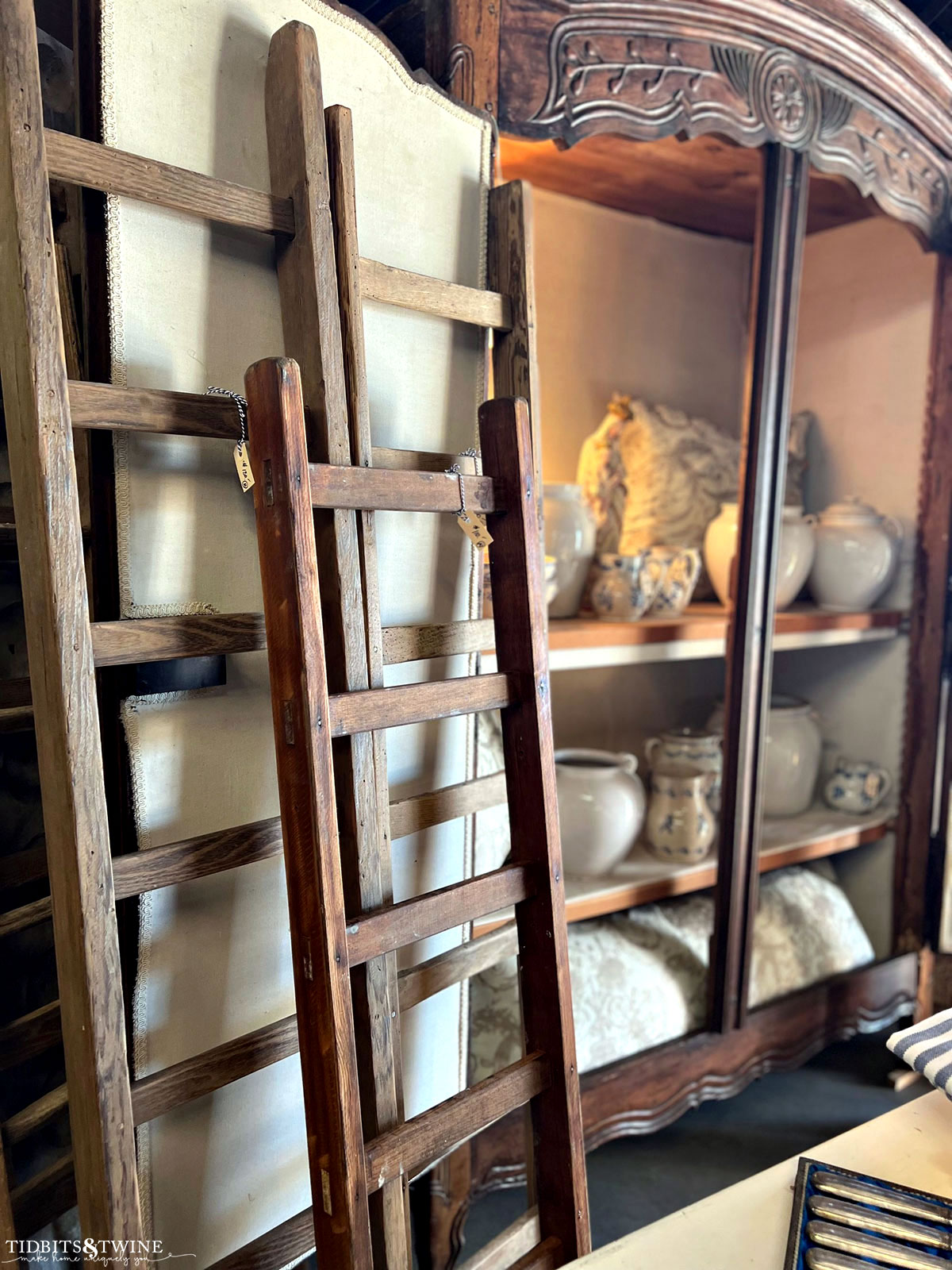 Antique French armoire lined with linen and full of antiques with old ladders leaning against the doors