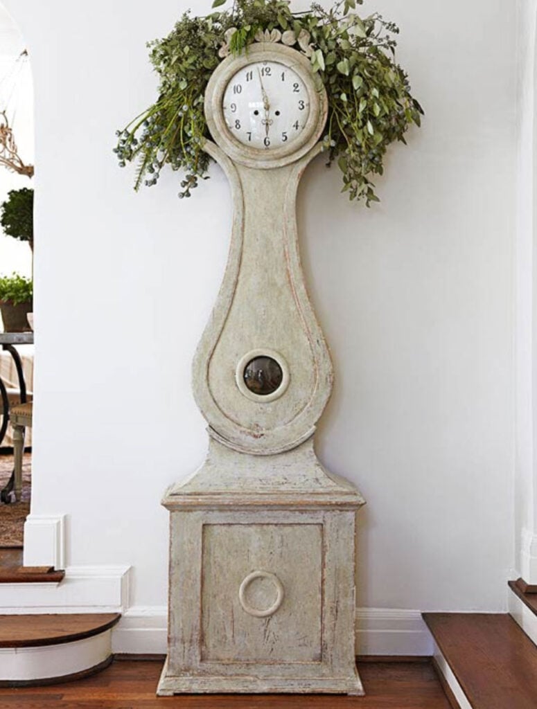 off white mora clock against white wall with greenery draped over the top