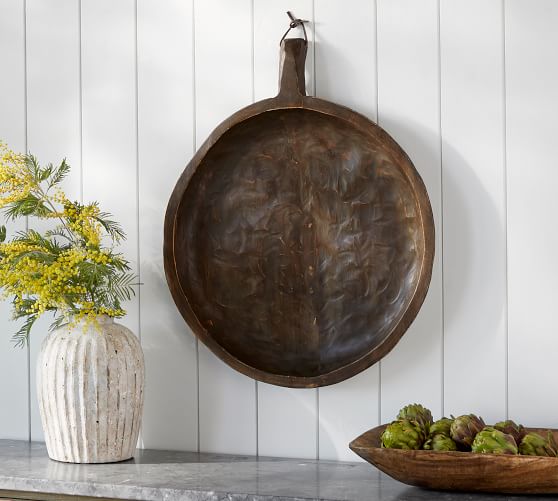 reproduction dough bowl hanging on a wall with smaller dough bowl holding artichokes on a table