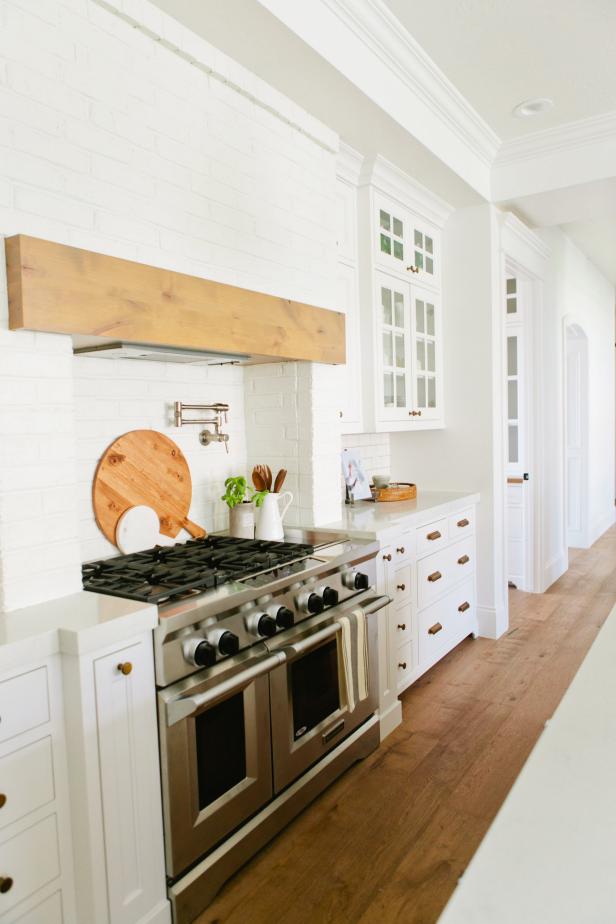 white kitchen with brick range hood and bread board displayed behind the stove