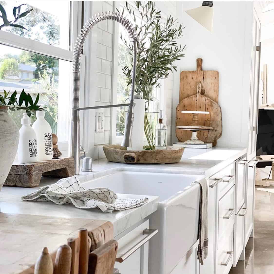 White kitchen with antique bread boards and dough bowls on display and a vase of olive branches