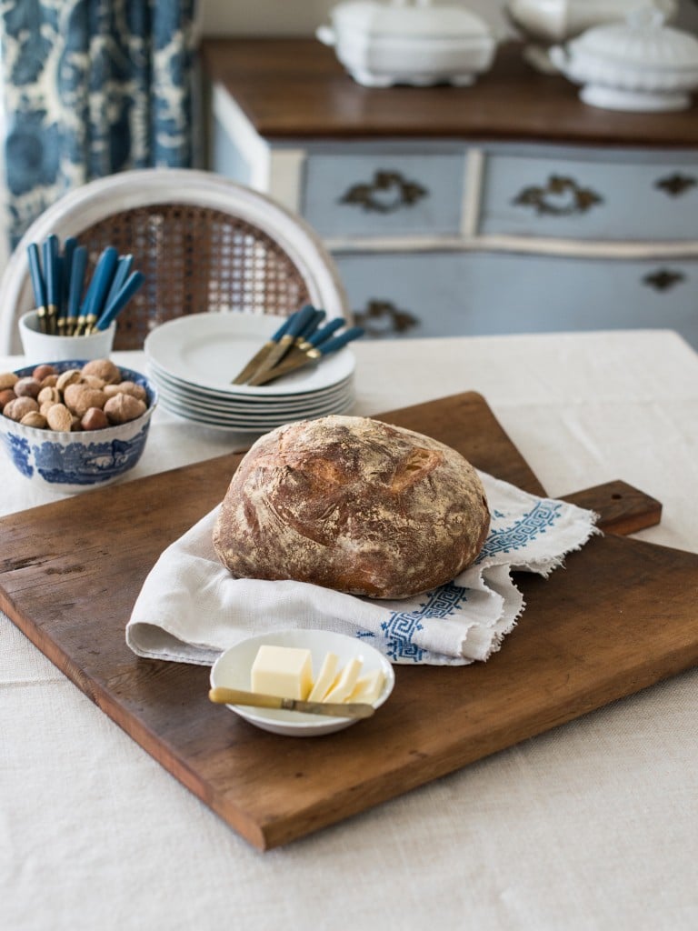 loaf of bread on an antique bread board on table with white and blue dishes