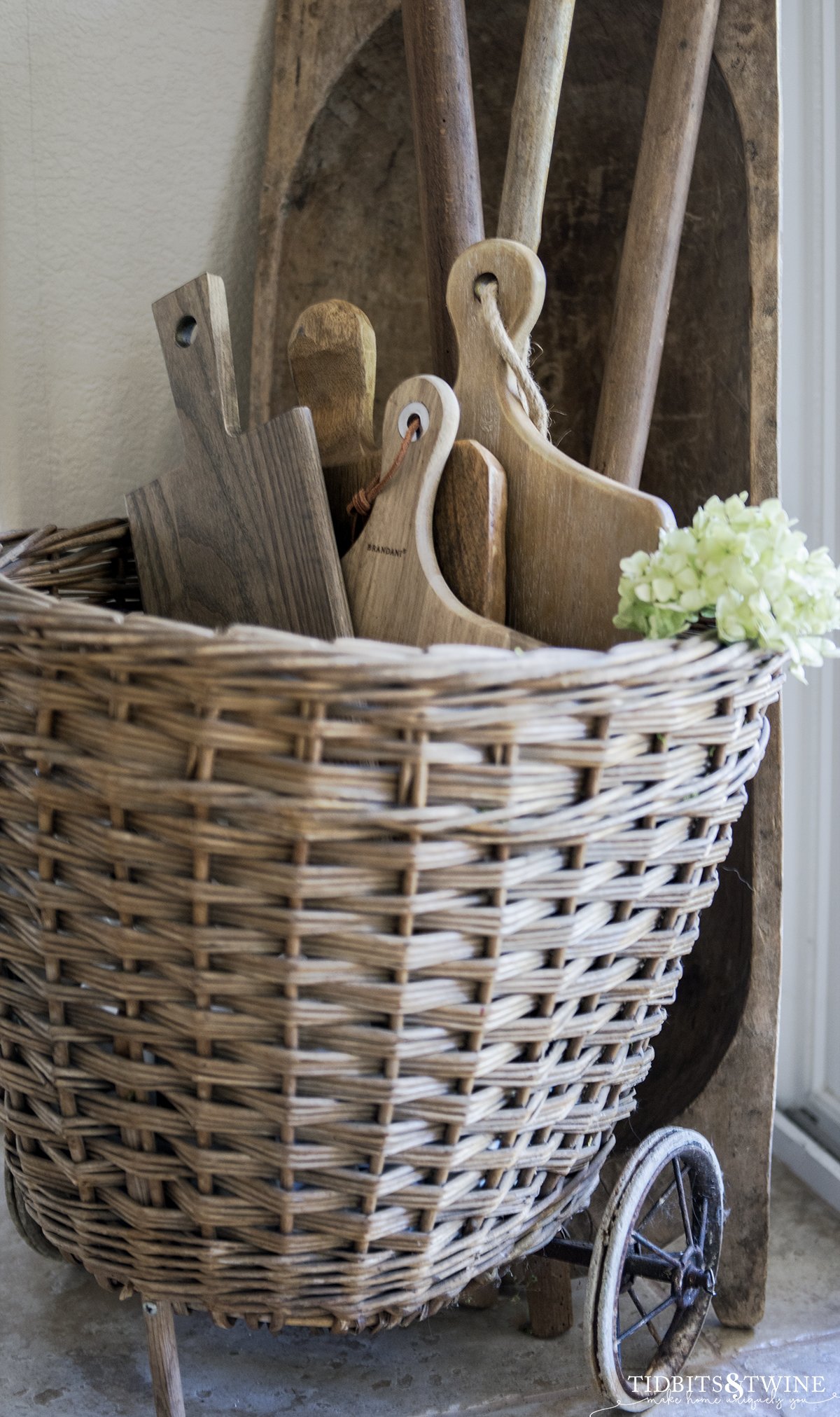 french market basket filled with antique bread board collection and dough bowl standing against wall