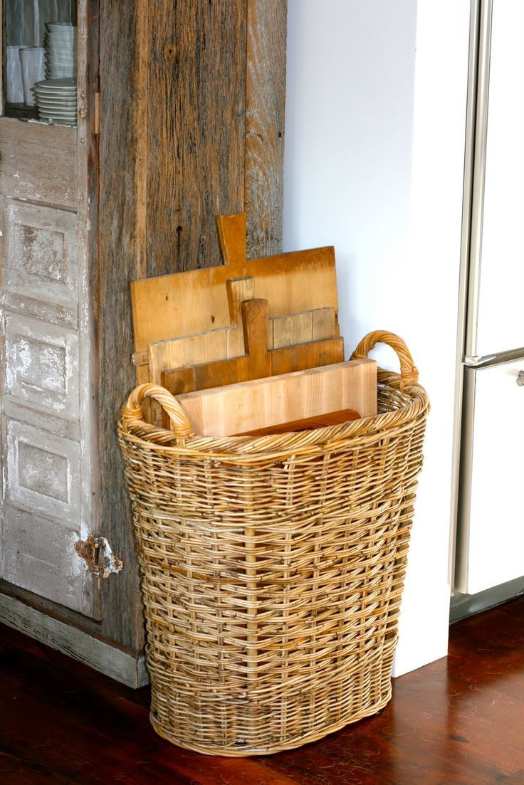 bread boards stacked vertically in a large tall basket on the floor next to rustic cabinet