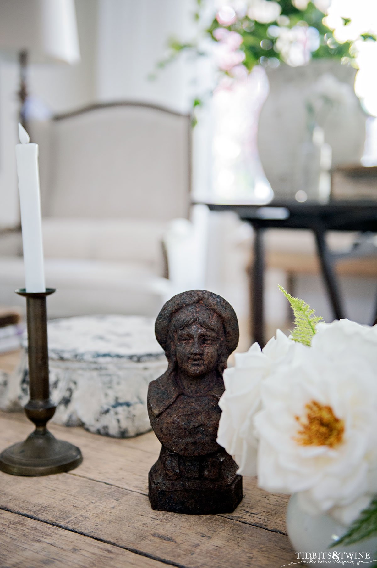 antique french andiron on coffee table next to white ironstone pot of white faux roses