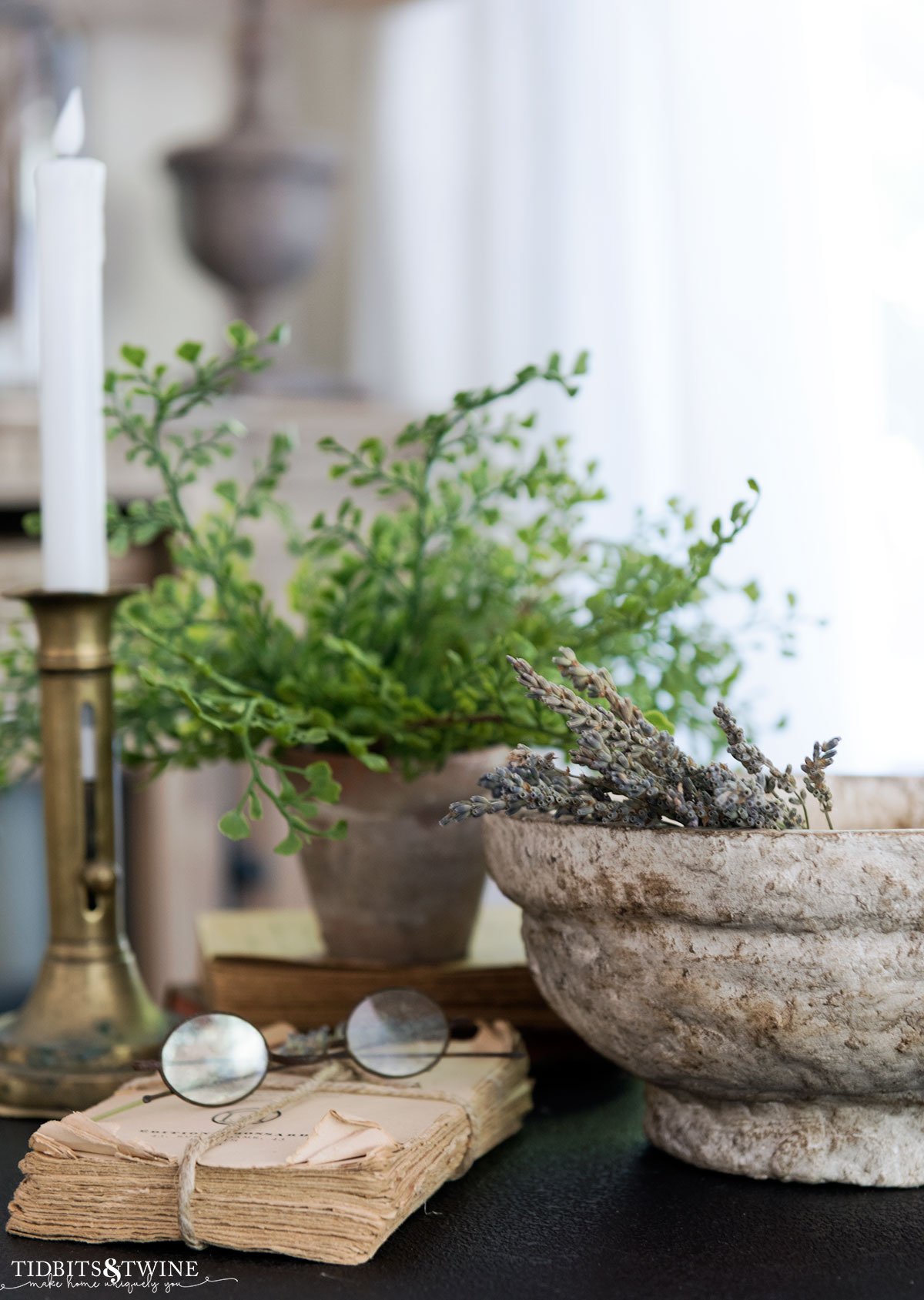 side table vignette with diy paper mache bowl holding lavender stems next to an old book with glasses plant and brass candlestick