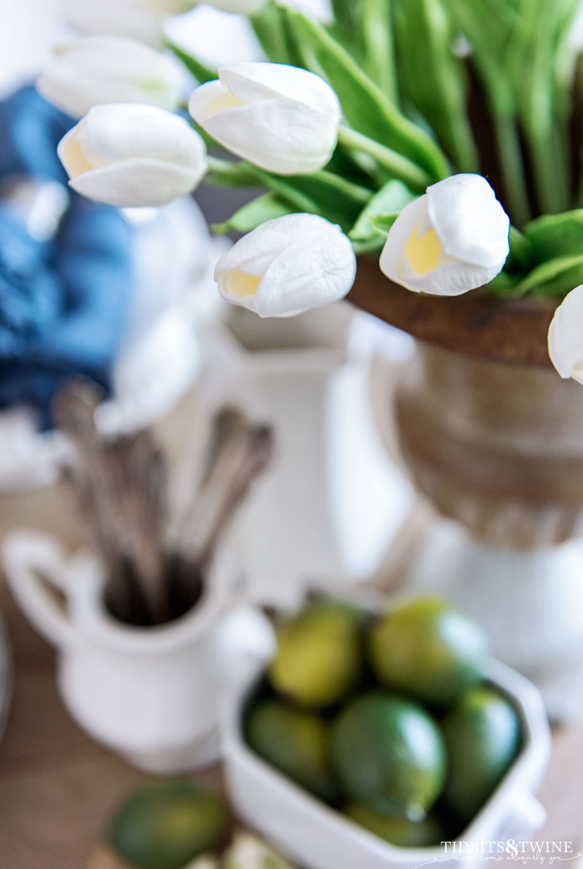 top down view of faux white tulips in a french urn with plates and utensils below