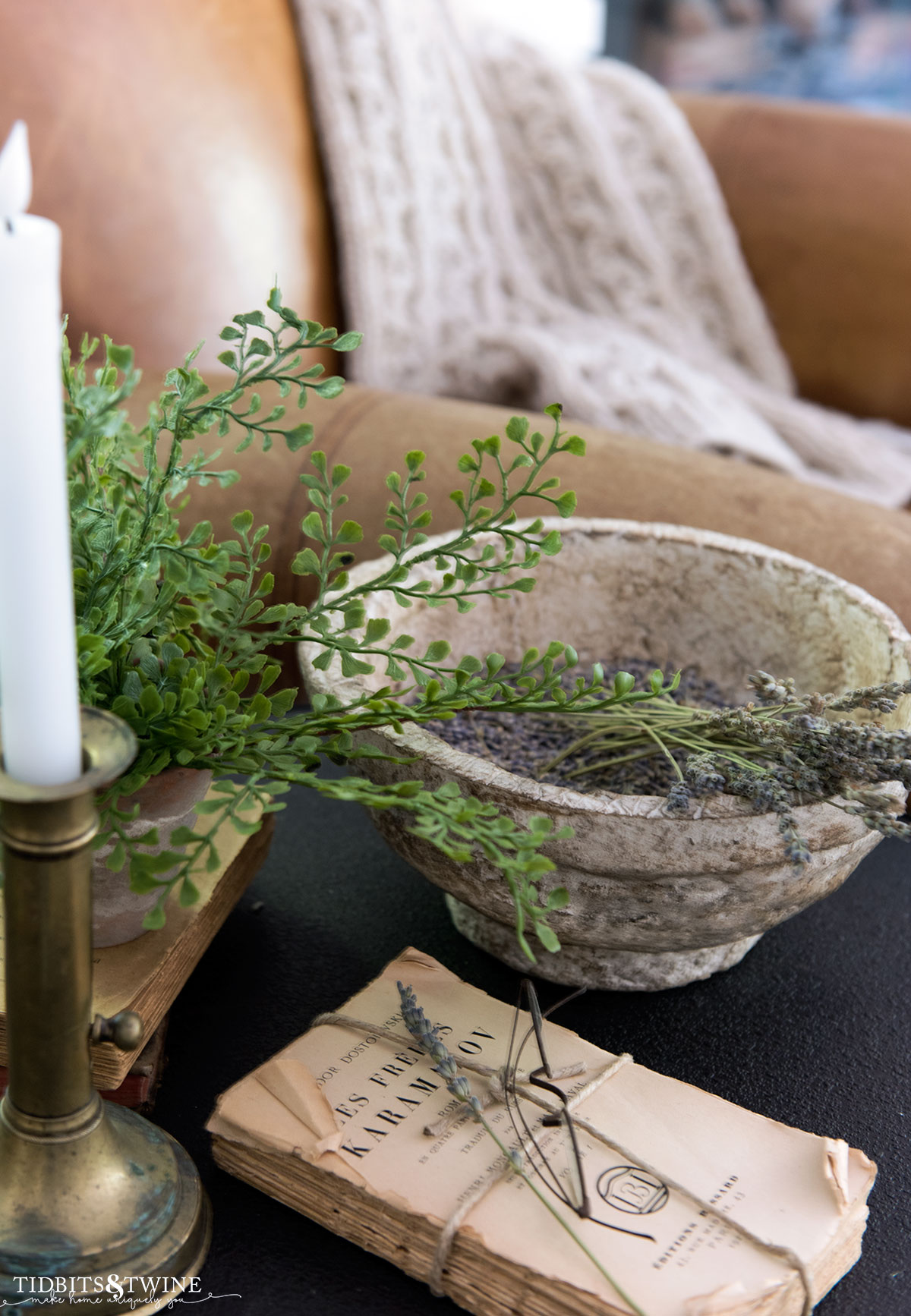 side table vignette with diy paper mache bowl holding lavender stems next to an old book and brass candlestick