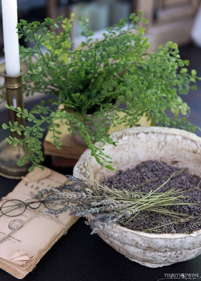 side table vignette with diy paper mache bowl holding lavender stems next to an old book with glasses and small green plant