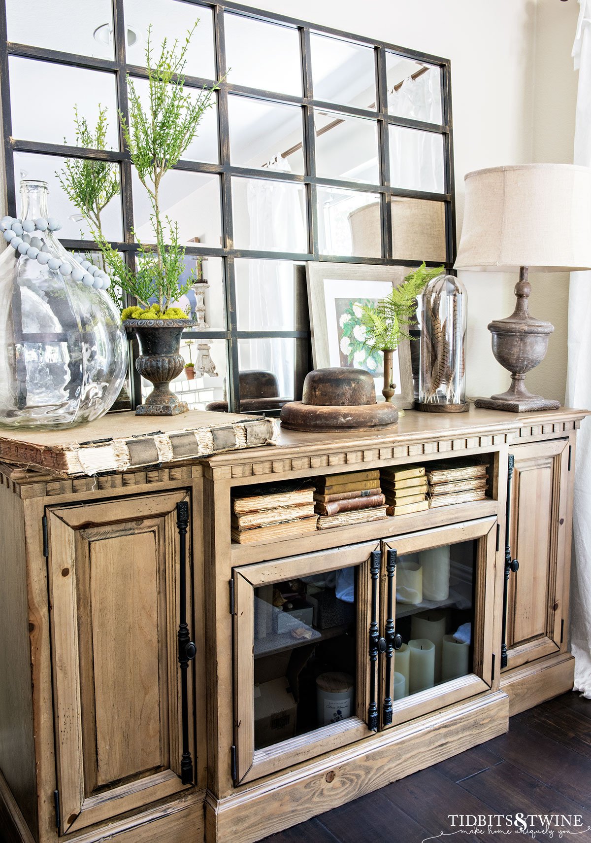 wooden console styled for spring with mirror above old books and myrtle topiary