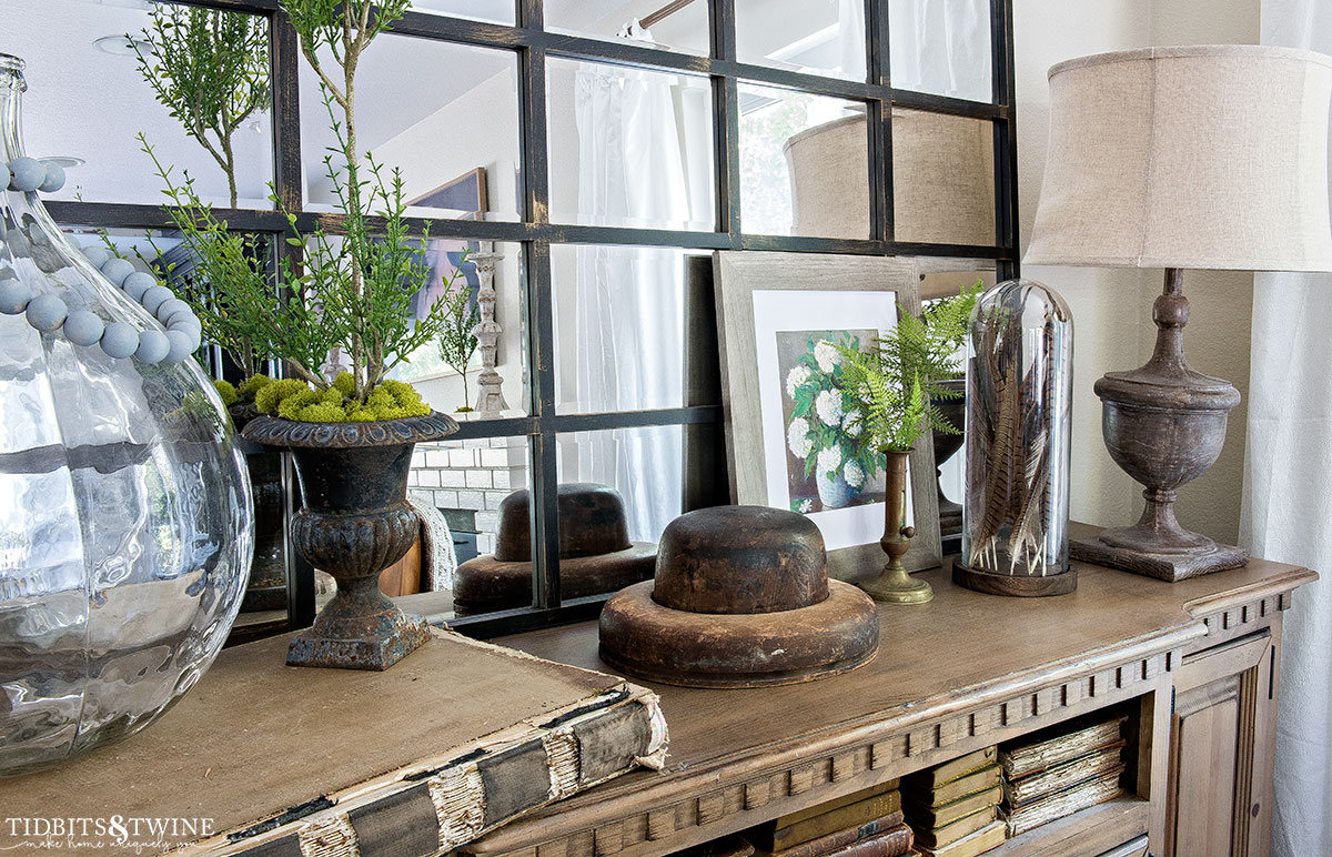 top of wooden console with paneled mirror on wall with myrtle topiary ferns and feathers