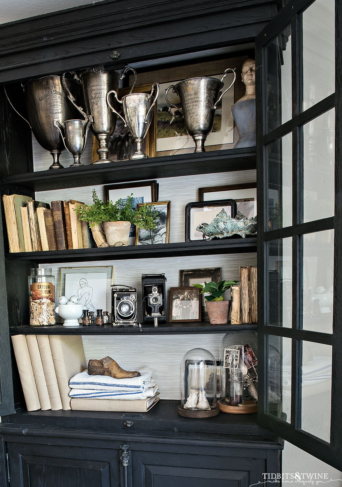 black cabinet with grasscloth wallpaper on the back styled with antiques for Spring