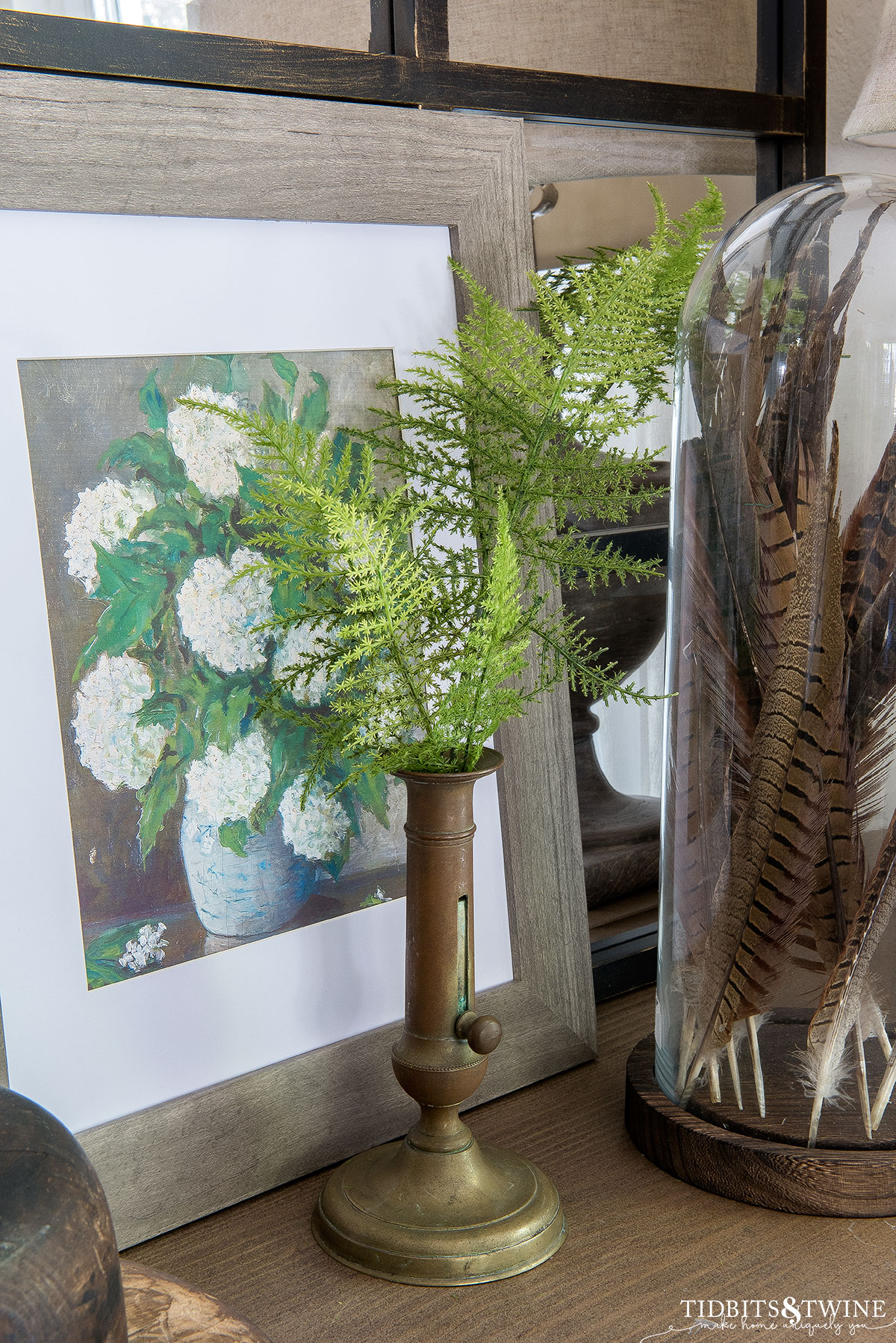 french brass antique candlestick with fern stems in it and framed spring art in background