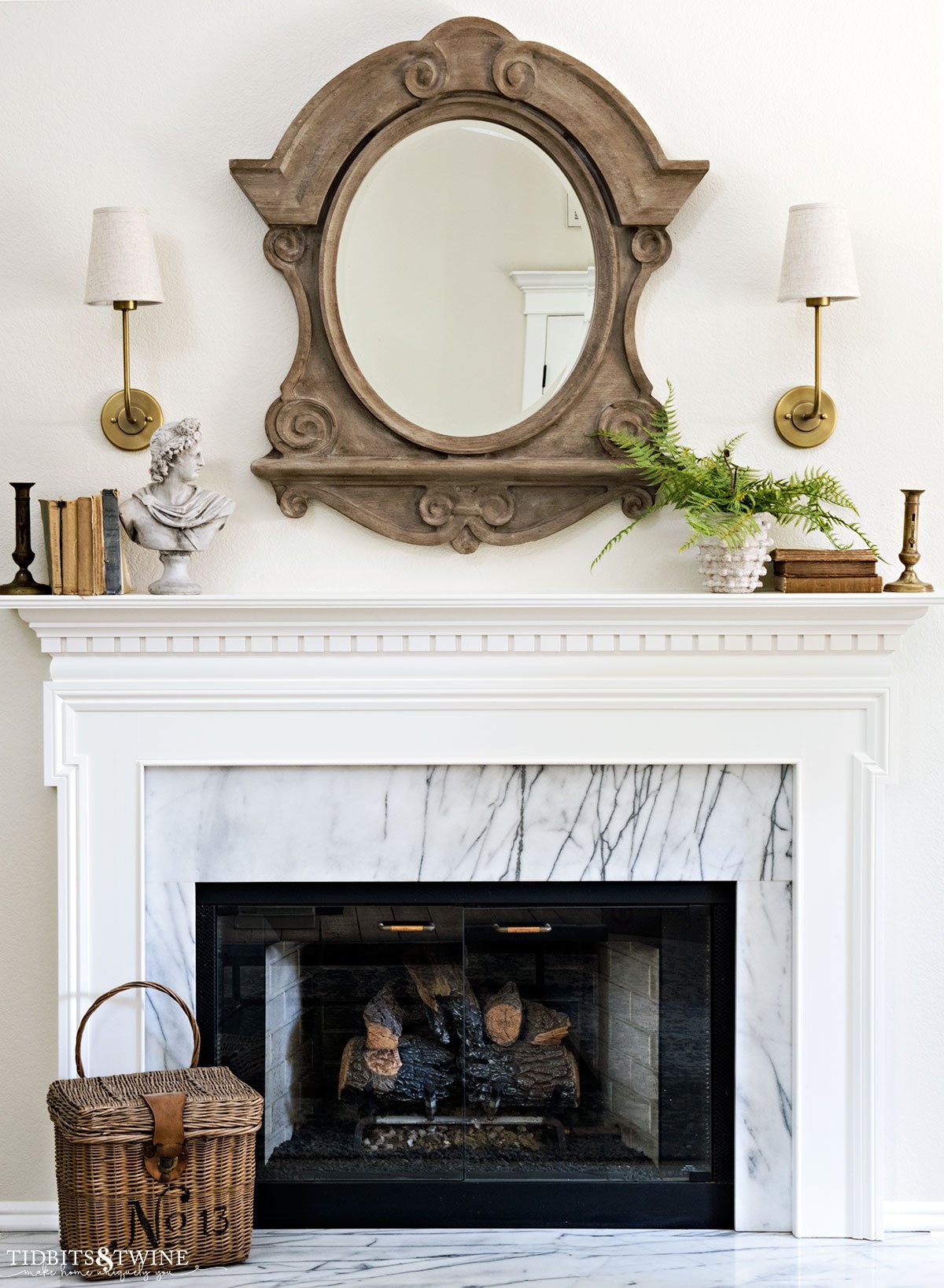white and marble fireplace decorated for spring with mansard mirror and brass sconces