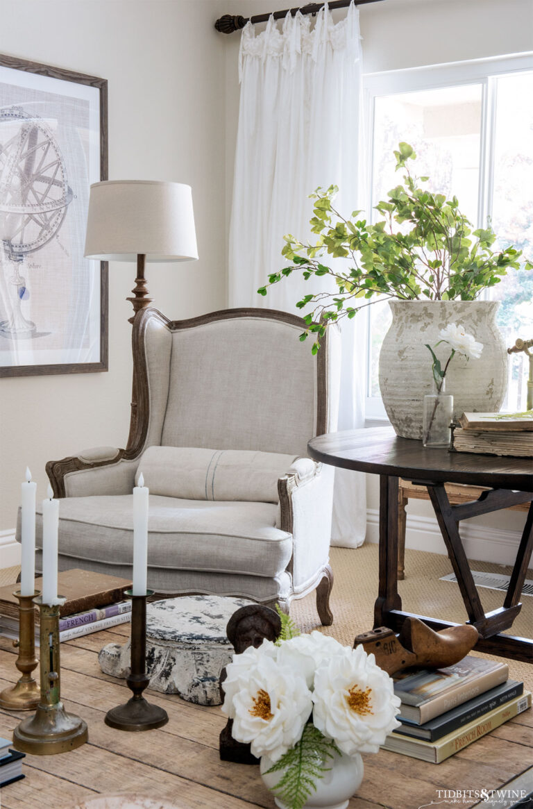 industrial coffee table in front of linen wingback chairs with antique wine tasting table in between