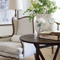 linen french wingback chair next to antique wine tasting table in spring living room