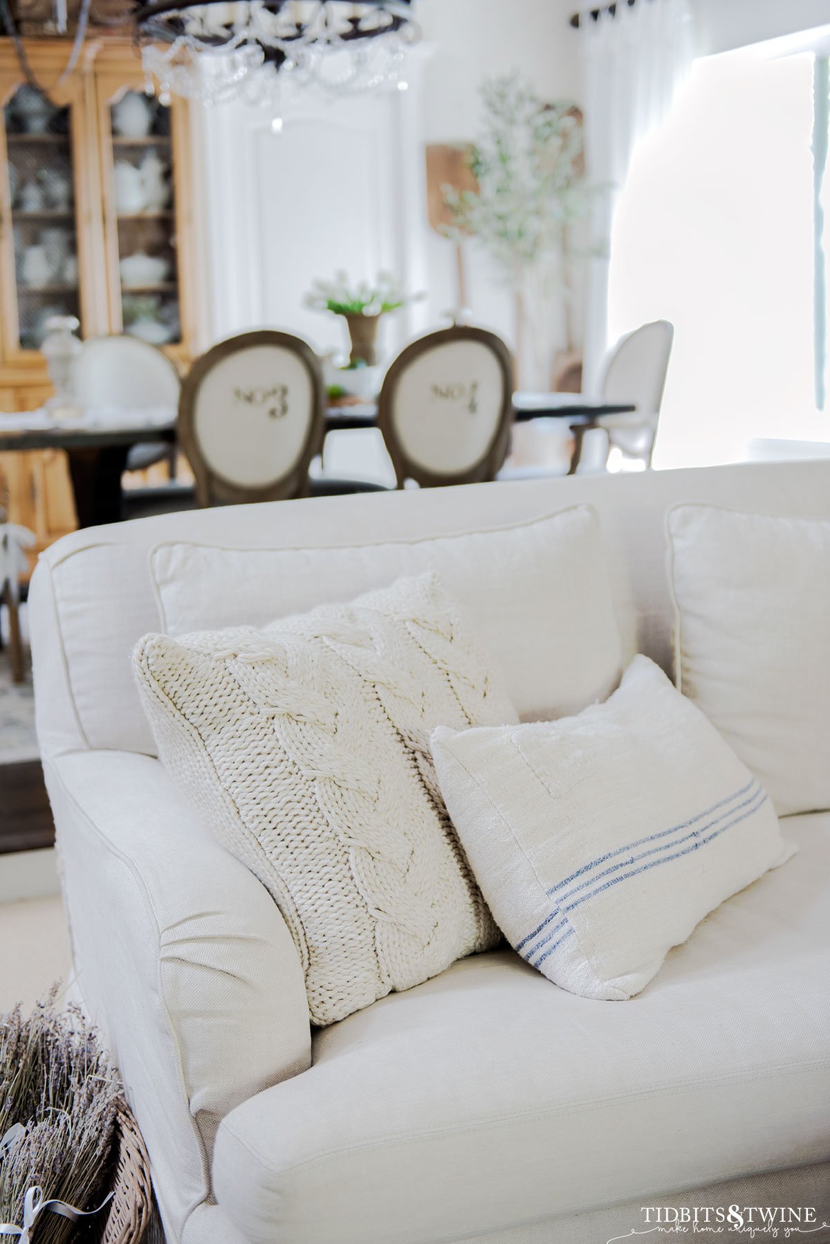 slipcovered linen sofa with blue stripe grain sack pillow and french dining room in background