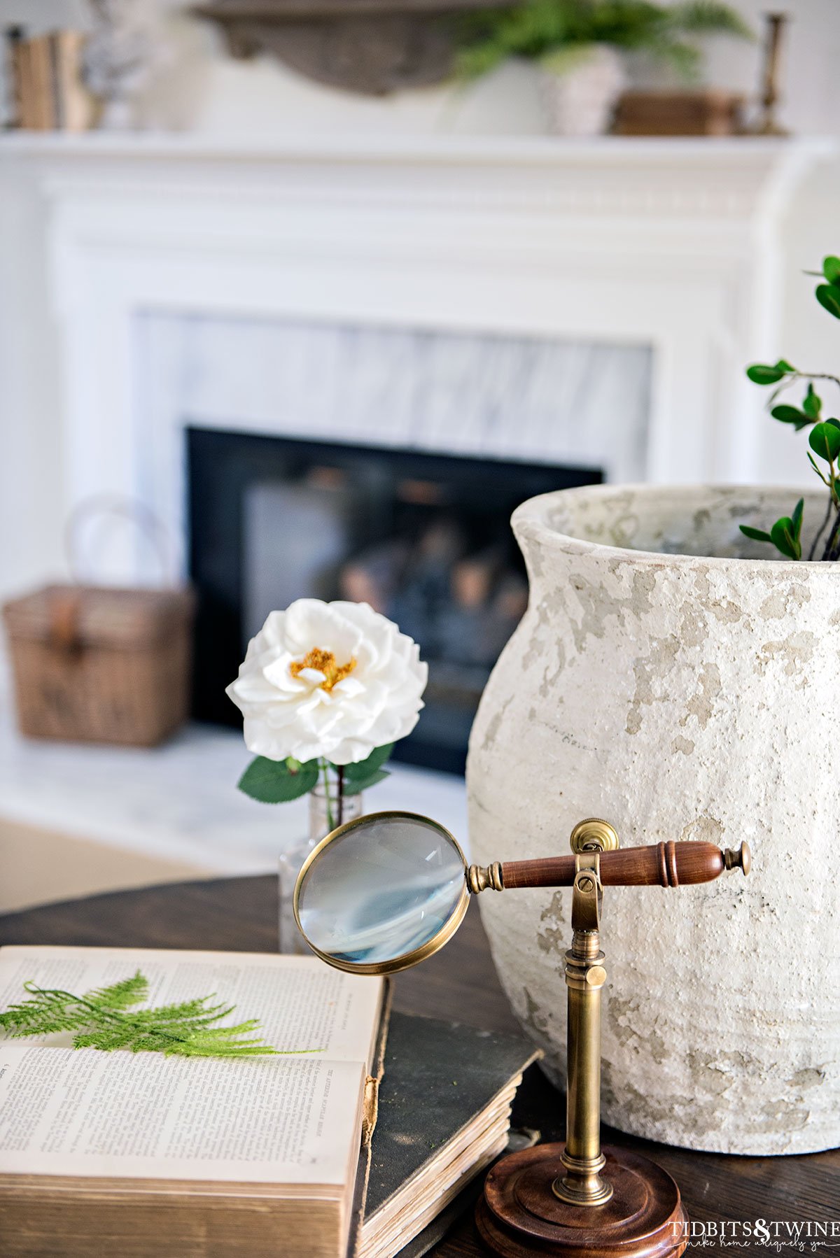 spring vignette on living room side table of old books flowers and magnifying glass with fireplace in background