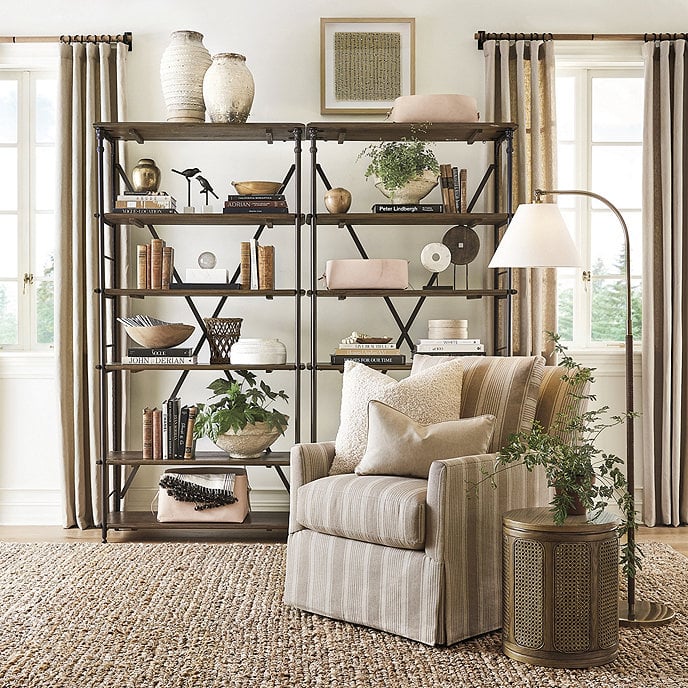 living room with two styled bookshelves in between windows and striped swivel chair