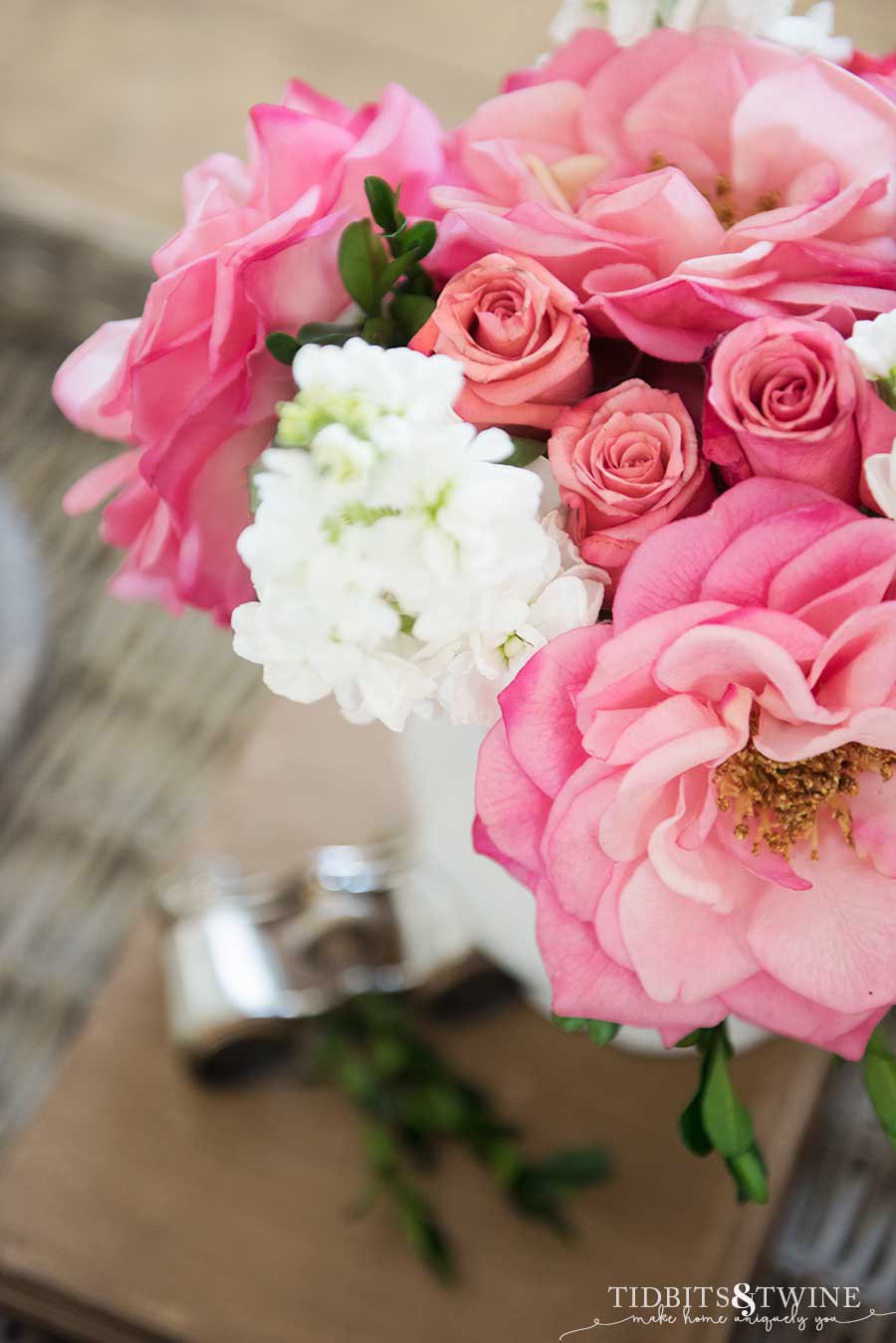 bouquet of pink rose buds and pink fake flowers with white stock and boxwood with opera glasses in the background