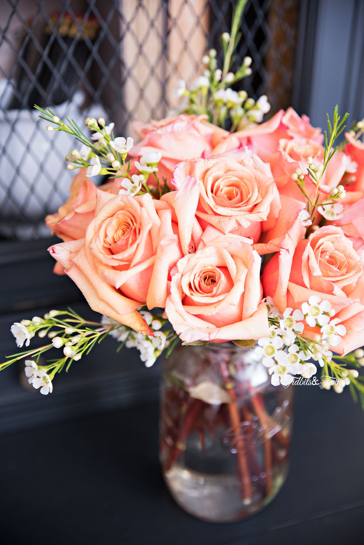 orange roses with white wax flowers in a mason jar on a black nightstand