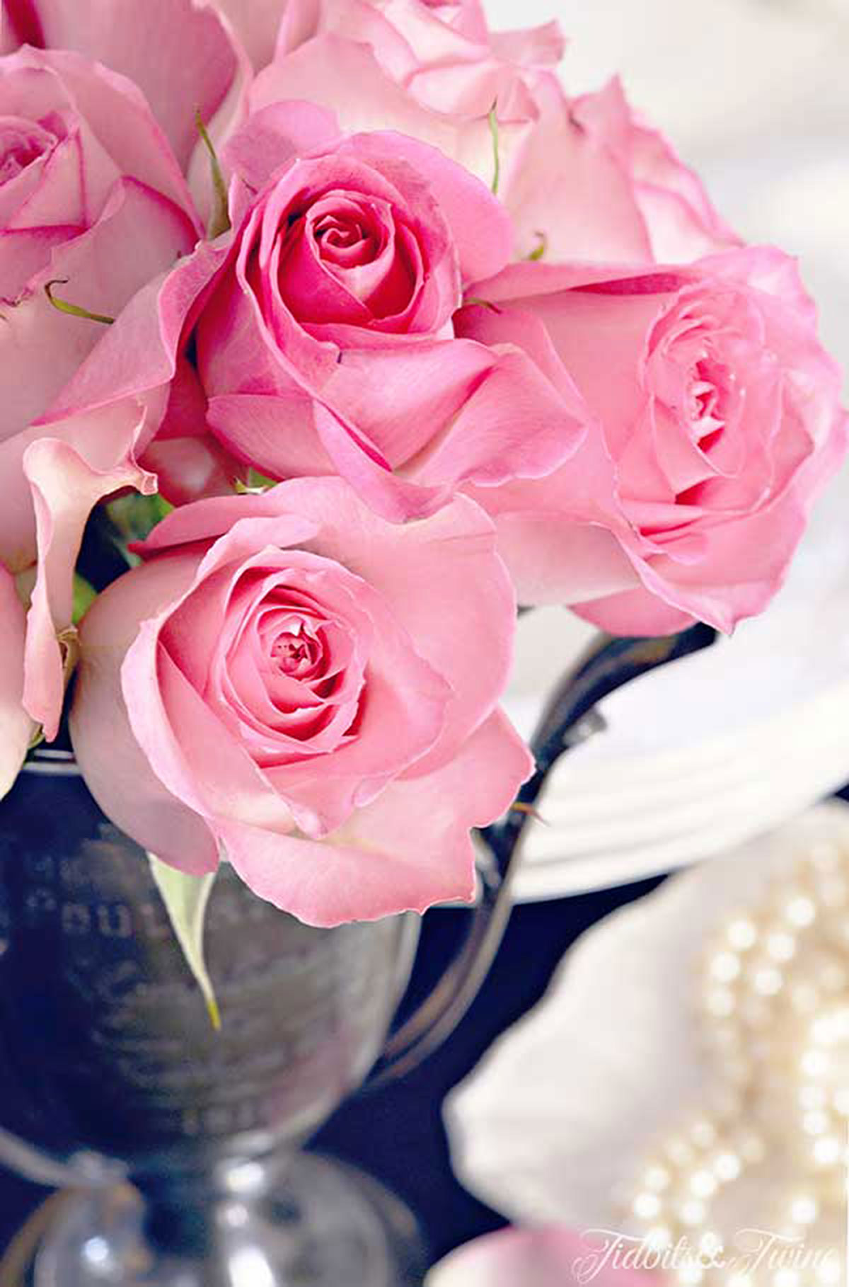 pink roses in an antique trophy with a plate holding a pearl necklace below