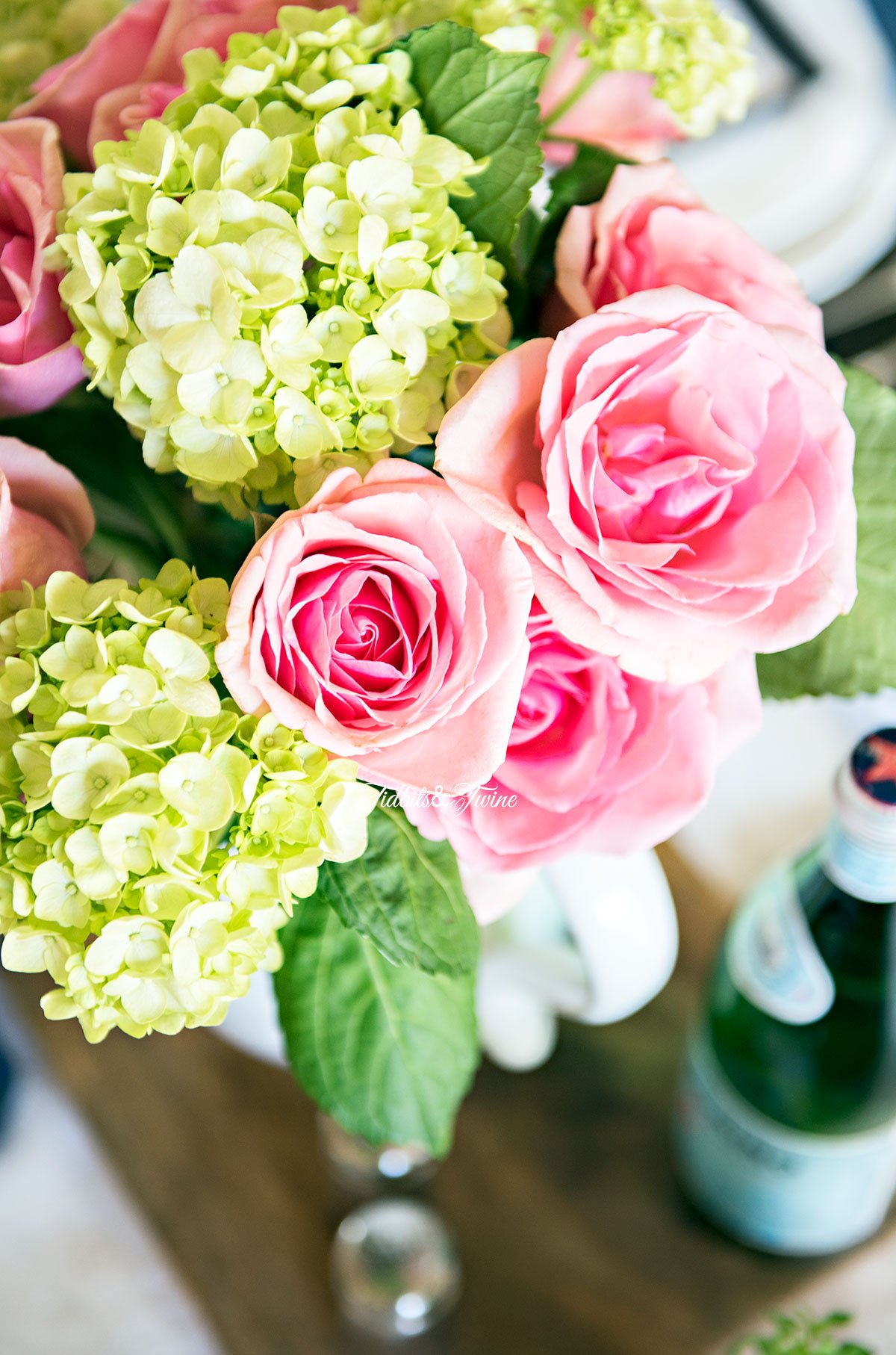 top down view of pink roses and green hydrangea on a dining table in a white pitcher