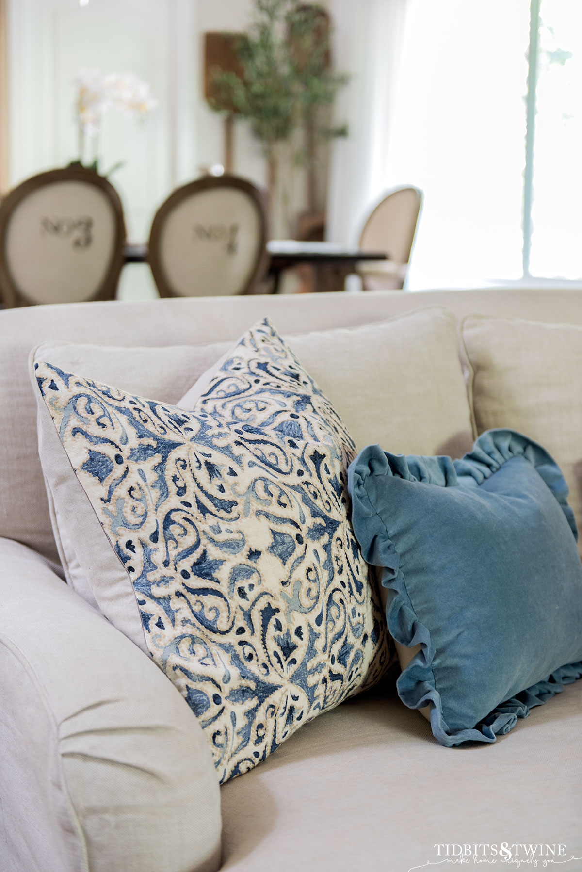 blue ruffle pillow in front of blue and white patterned pillow on belgian linen sofa with dining table in background