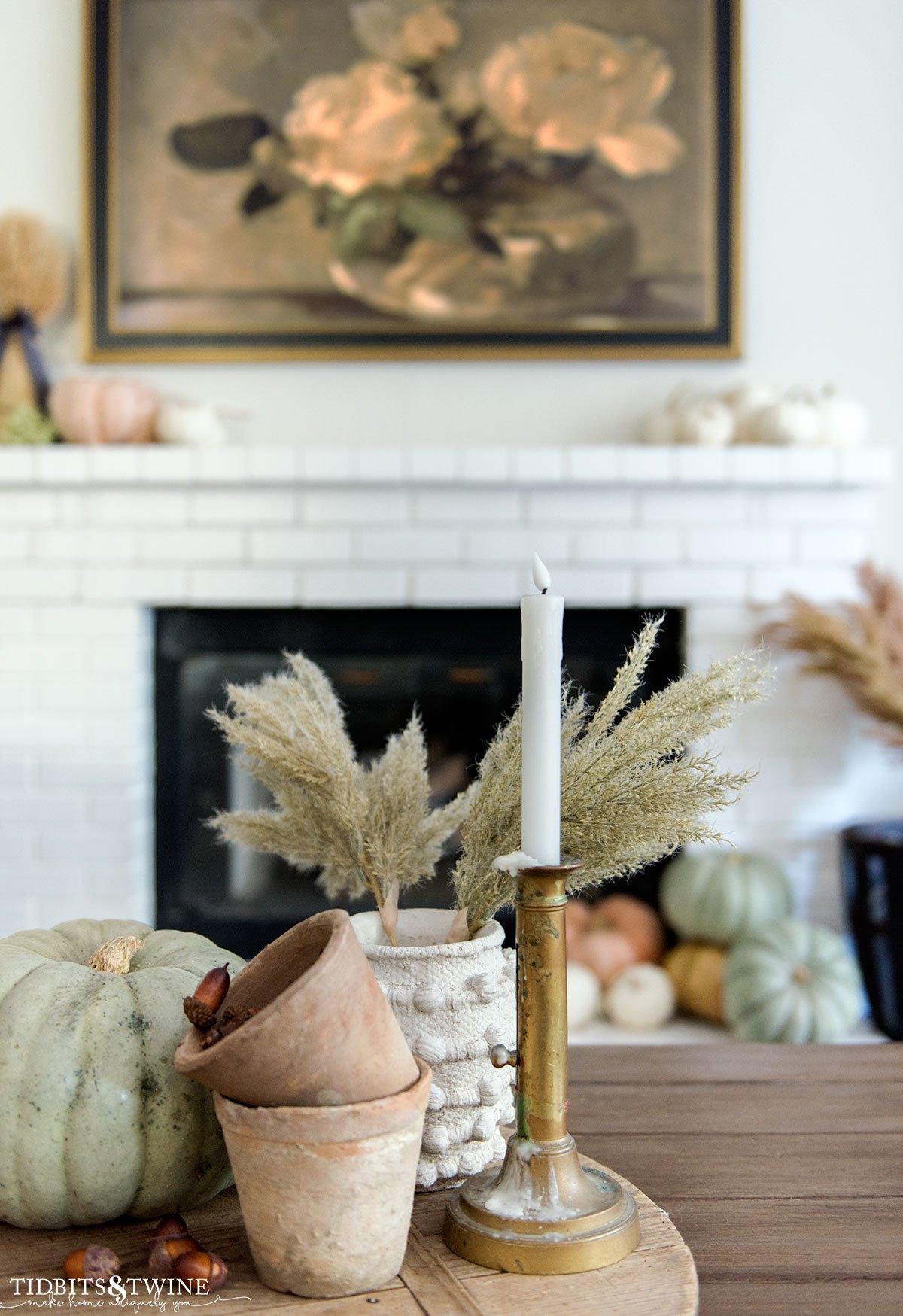 fall coffee table centerpiece with brass candlestick, small terracotta pots, green pumpkin and vase with grasses and fireplace in background