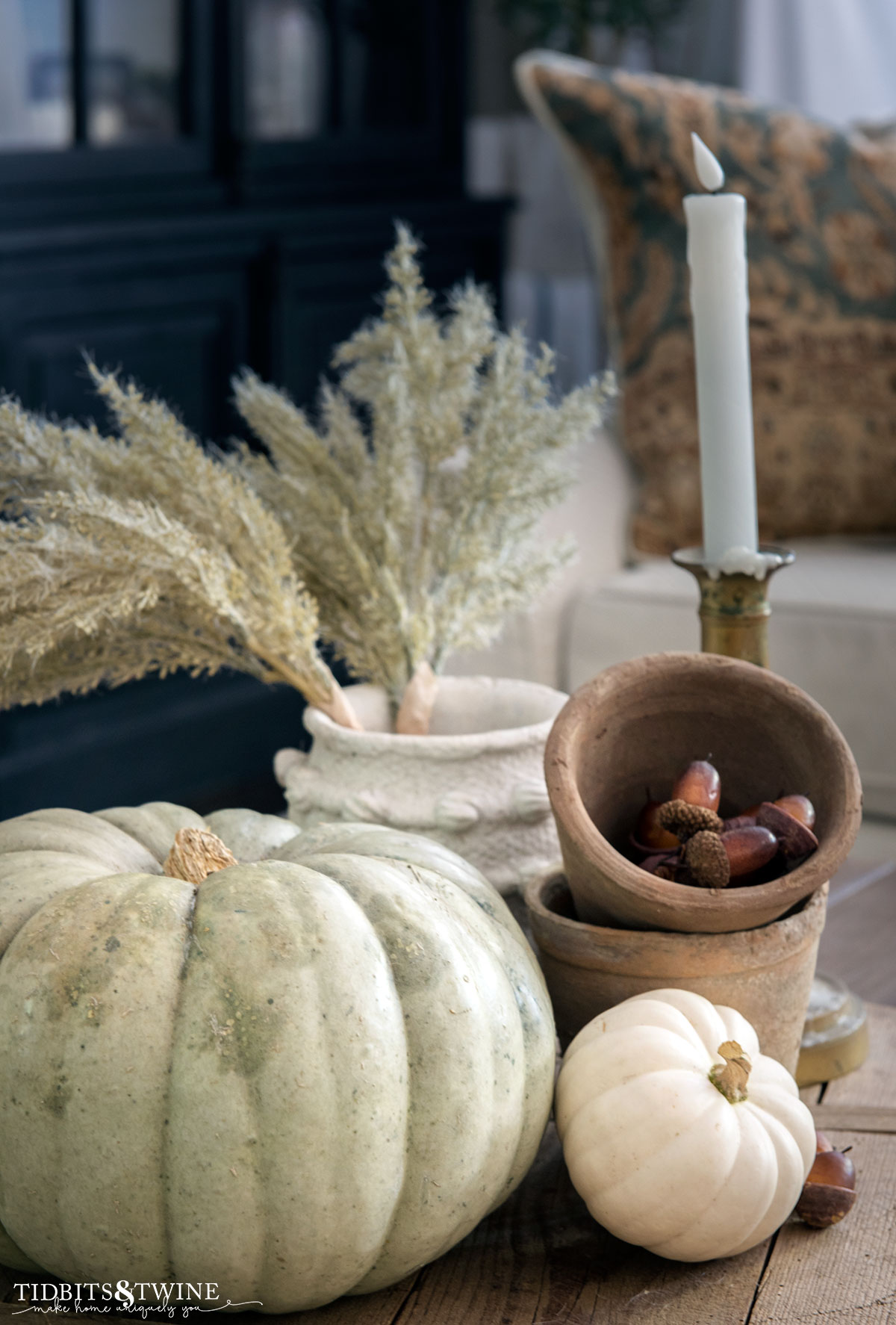 coffee table centerpiece with green pumpkin, brass candlestick, terracotta pots, acorns and grass stems