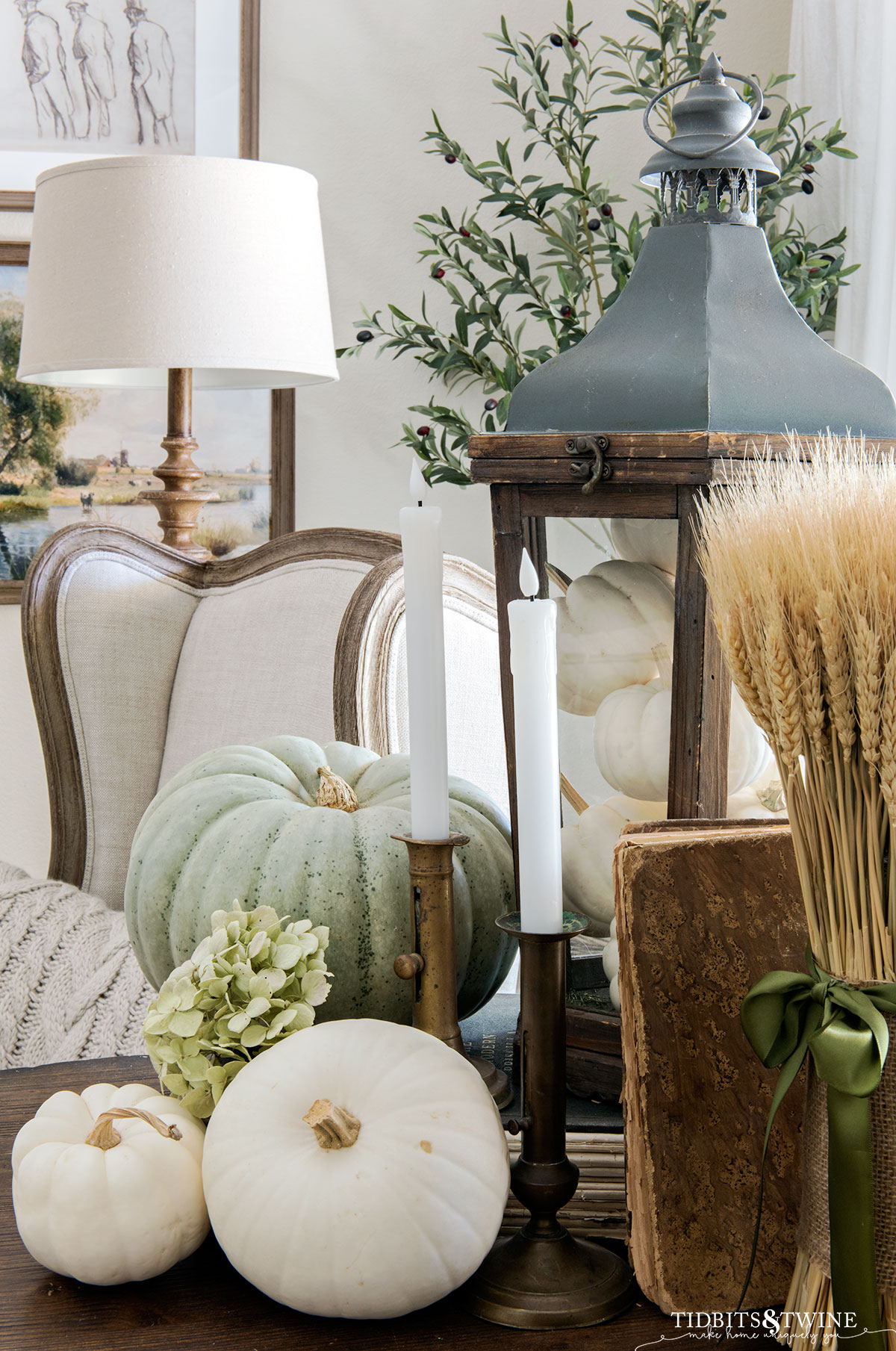 side table vignette with wooden lantern full of white pumpkins, wheat bundle, and pumpkins next to wingback bergere chair