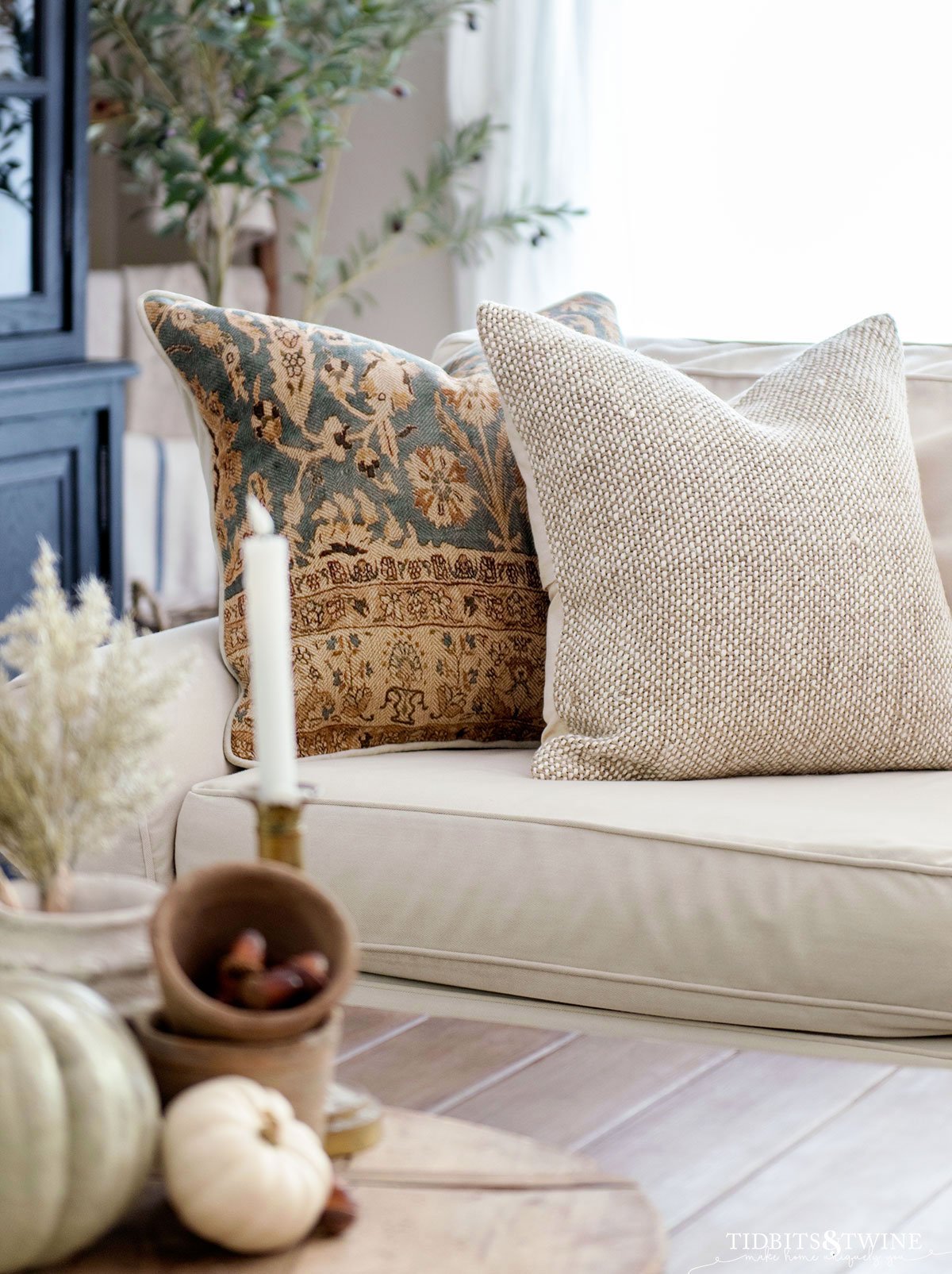 beige textured linen pillow in front of blue and terracotta patterned pillow on white slipcovered sofa in fall family room