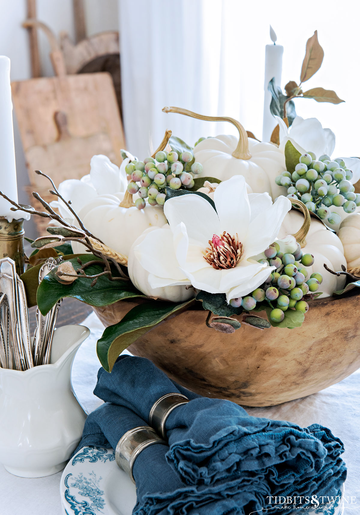dough bowl centerpiece with white pumpkins and magnolia flowers with blue ruffle napkins and utensiles at base of bowl