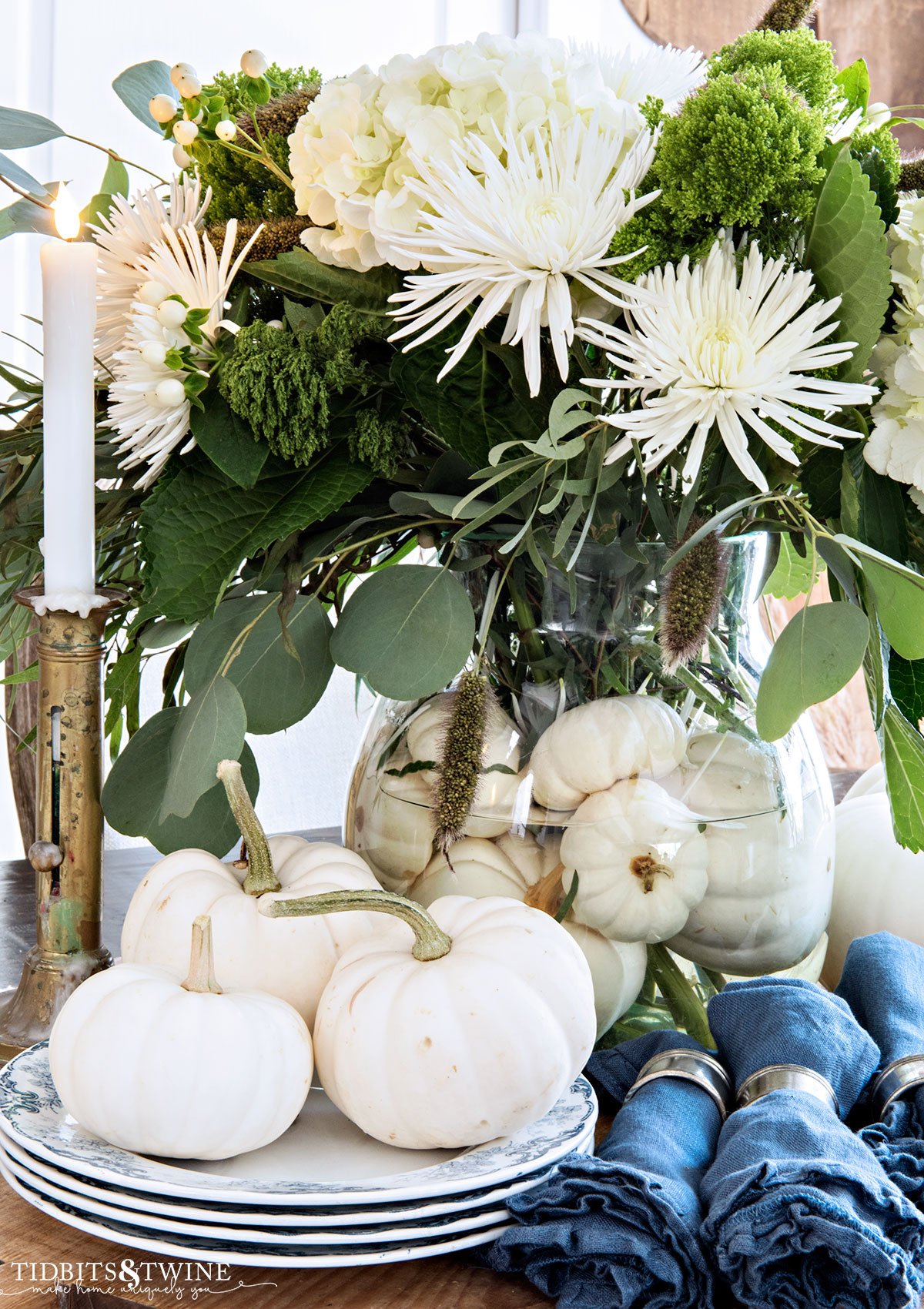 fall green and white flower arrangement with white pumpkins vase filler and white pumpkins and blue napkins next to vase