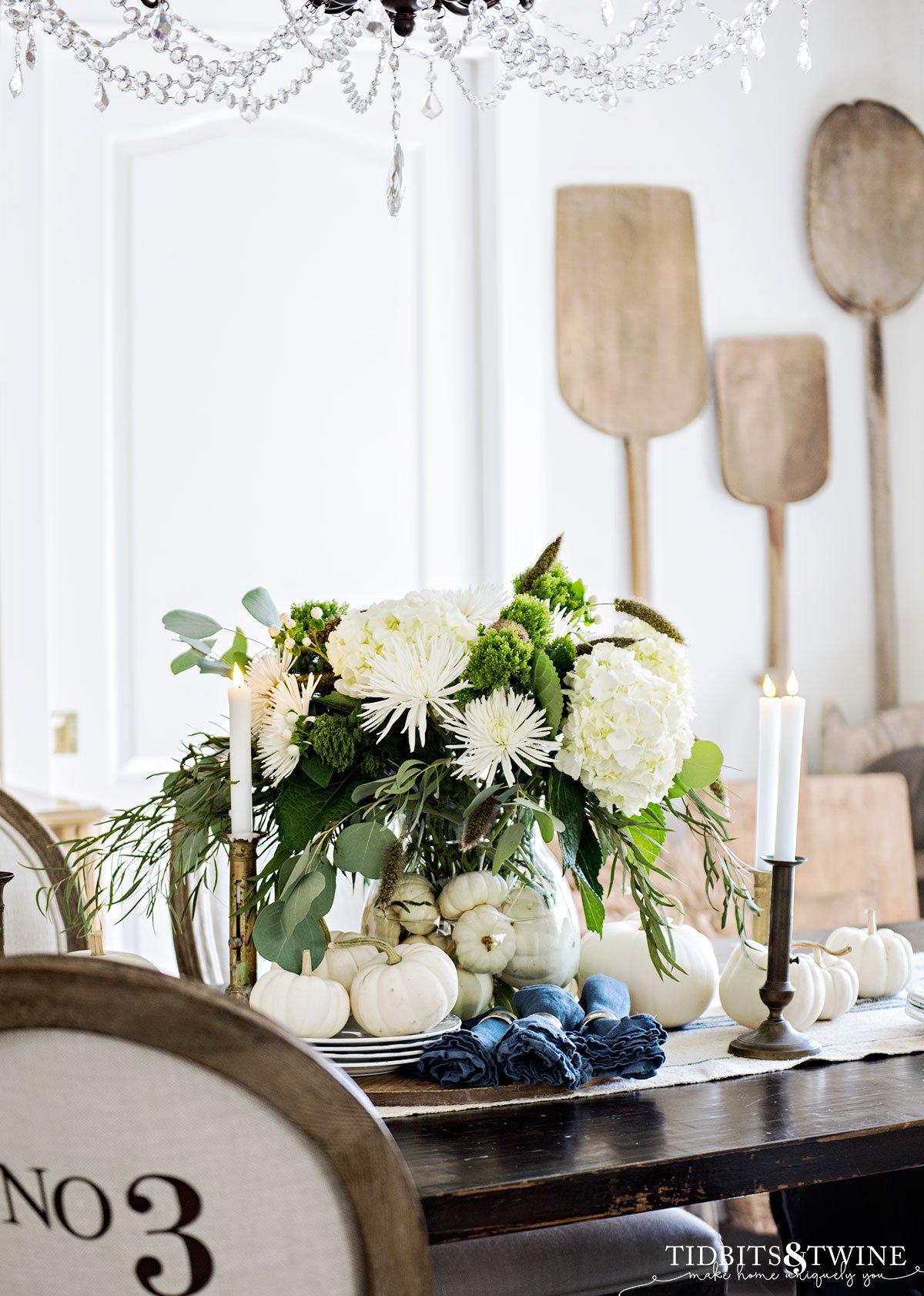 Neutral dining room tablescape with large fall flower arrangement, white pumpkins, and candles
