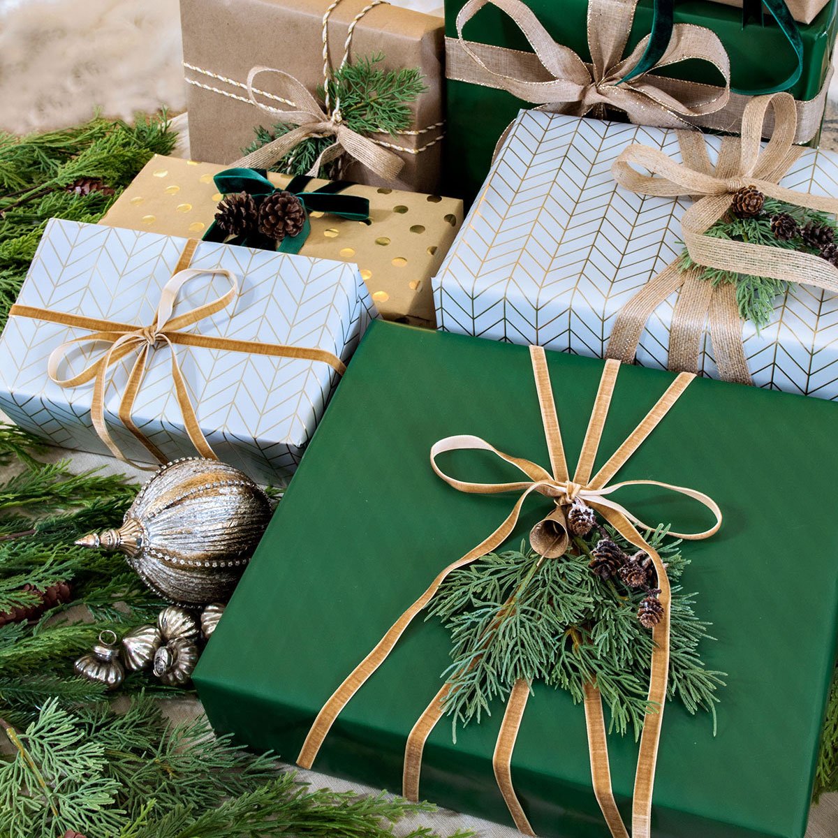 green white and gold wrapped christmas presents underneath a tree with bits of faux greenery and velvet ribbon
