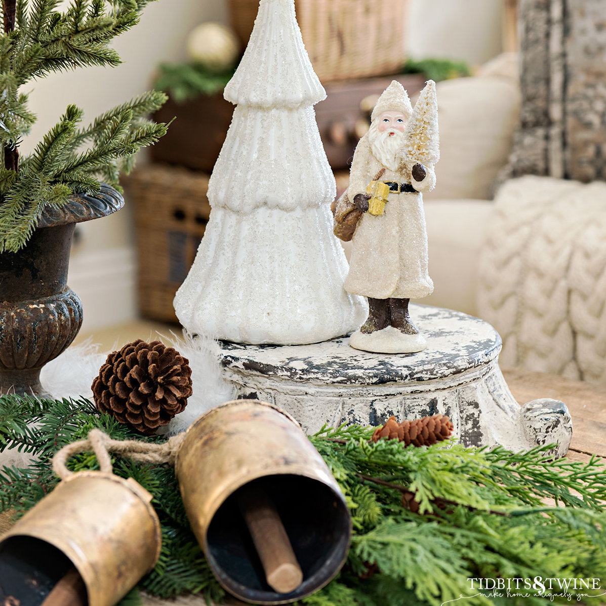 closeup of a white christmas tree with a white santa next to it and greenery at the base